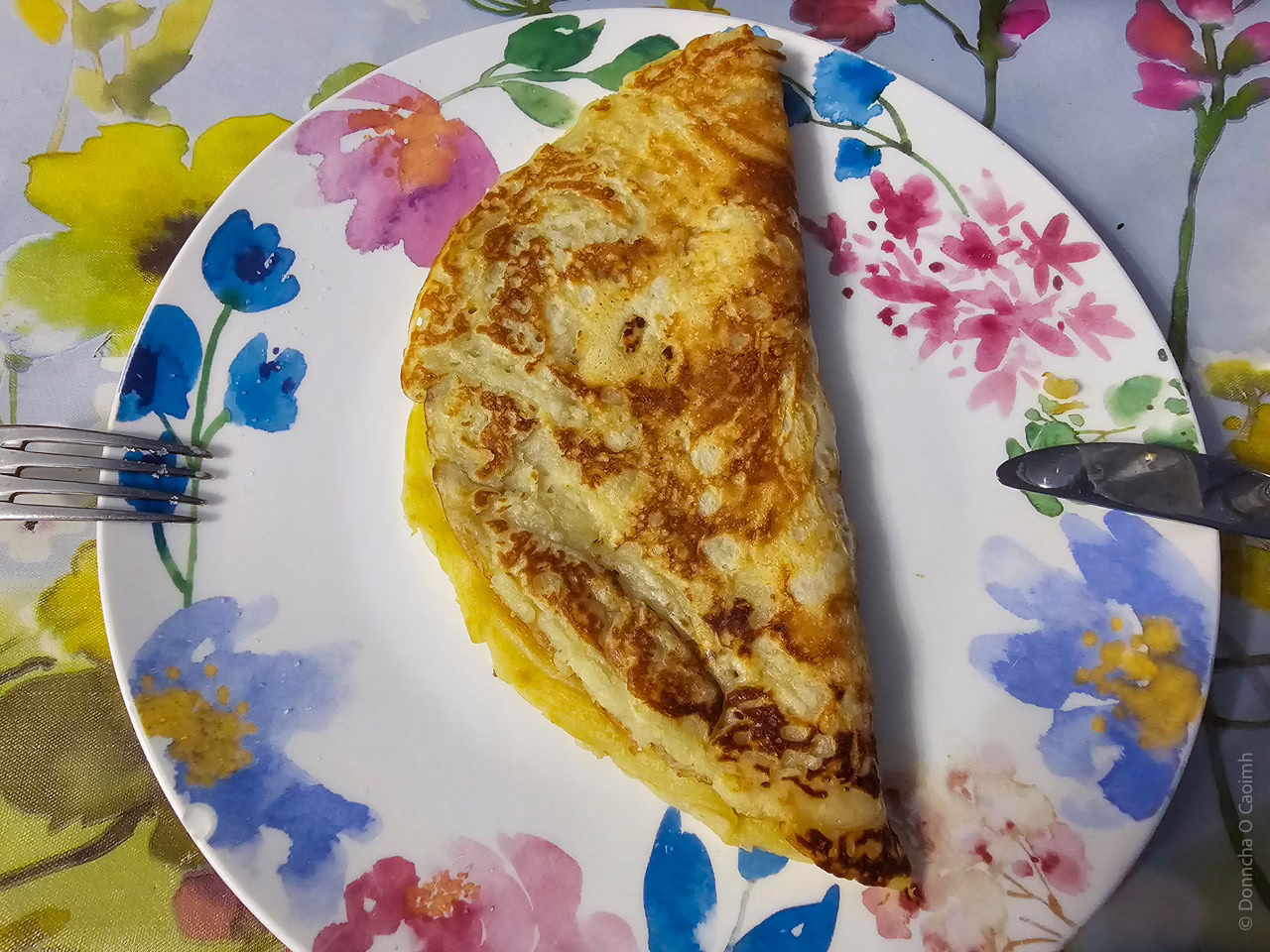 A folded pancake on a plate, with a knife and fork.